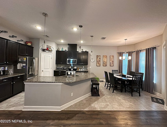 kitchen featuring dark stone countertops, appliances with stainless steel finishes, sink, pendant lighting, and an island with sink