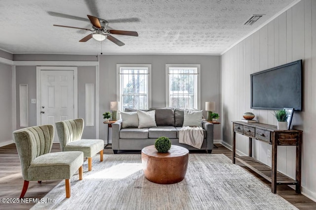 living room with ceiling fan, dark wood-type flooring, ornamental molding, and a textured ceiling