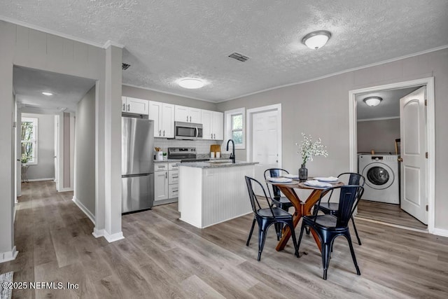 kitchen with crown molding, washer / dryer, stainless steel appliances, and white cabinets