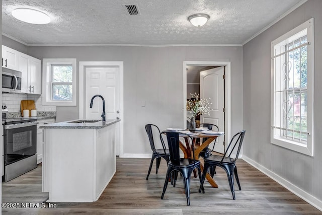 interior space featuring sink, appliances with stainless steel finishes, light stone counters, white cabinets, and a center island with sink