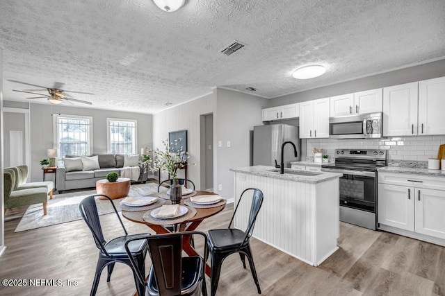 kitchen with appliances with stainless steel finishes, white cabinetry, sink, a kitchen island with sink, and light stone countertops