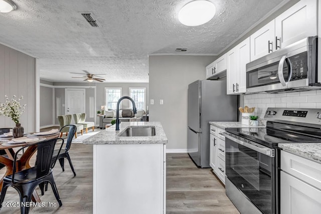 kitchen with sink, white cabinetry, appliances with stainless steel finishes, an island with sink, and light stone countertops