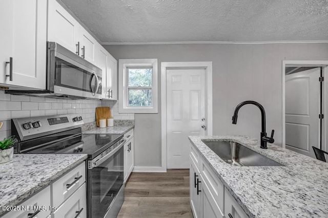 kitchen with appliances with stainless steel finishes, white cabinetry, sink, dark hardwood / wood-style flooring, and light stone counters