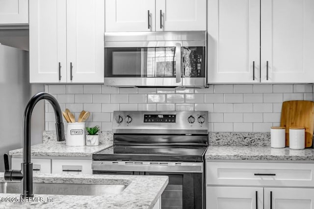 kitchen featuring white cabinetry, appliances with stainless steel finishes, light stone countertops, and decorative backsplash