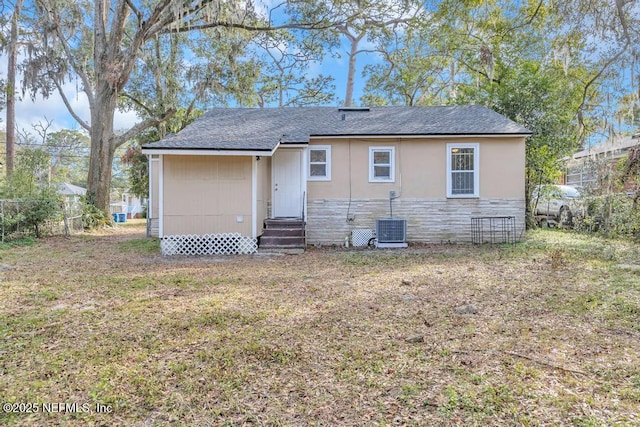 rear view of property featuring central AC unit and a lawn