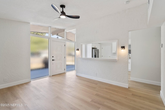 unfurnished living room featuring vaulted ceiling, a textured ceiling, ceiling fan, and light wood-type flooring