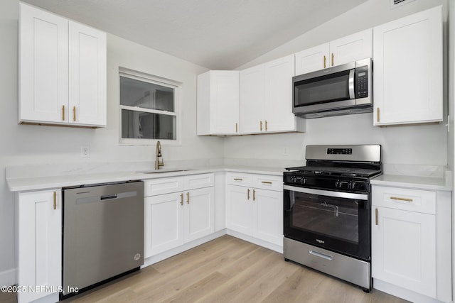 kitchen featuring lofted ceiling, appliances with stainless steel finishes, sink, and white cabinets