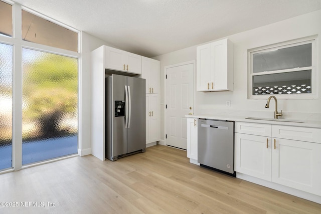 kitchen featuring appliances with stainless steel finishes, sink, light hardwood / wood-style flooring, and white cabinets