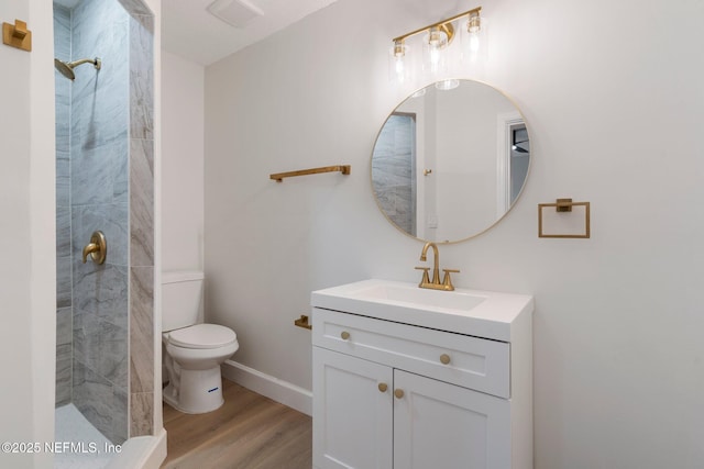 bathroom with hardwood / wood-style flooring, tiled shower, vanity, and toilet