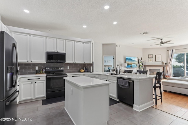 kitchen featuring black appliances, white cabinetry, sink, a center island, and kitchen peninsula