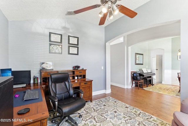 office area with ceiling fan, hardwood / wood-style flooring, vaulted ceiling, and a textured ceiling