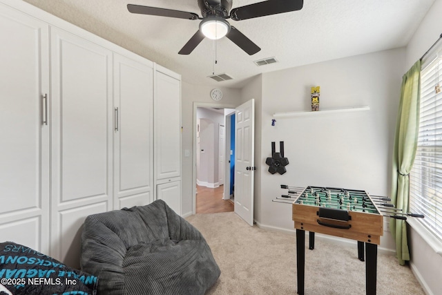 playroom with light carpet, ceiling fan, and a textured ceiling