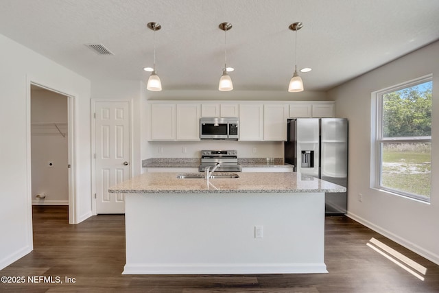 kitchen with stainless steel appliances, white cabinetry, a center island with sink, and decorative light fixtures