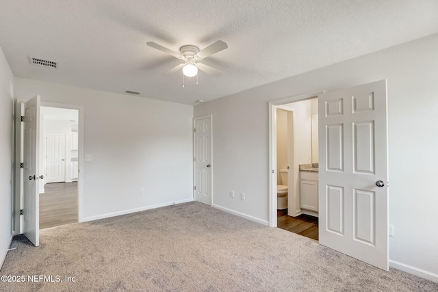 unfurnished bedroom featuring ensuite bath, a textured ceiling, and dark colored carpet