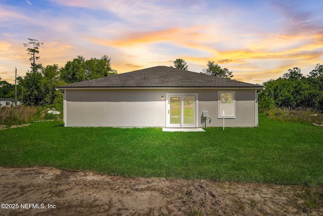 back house at dusk featuring a lawn