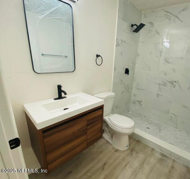 bathroom with vanity, wood-type flooring, toilet, and a tile shower