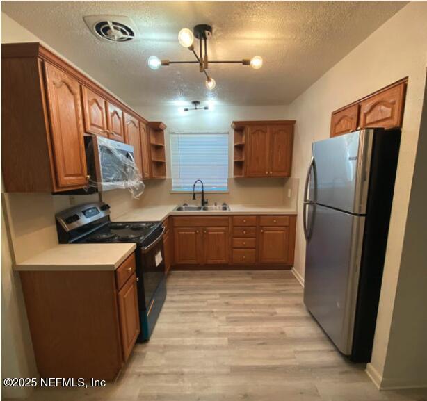 kitchen with sink, light wood-type flooring, a textured ceiling, and appliances with stainless steel finishes