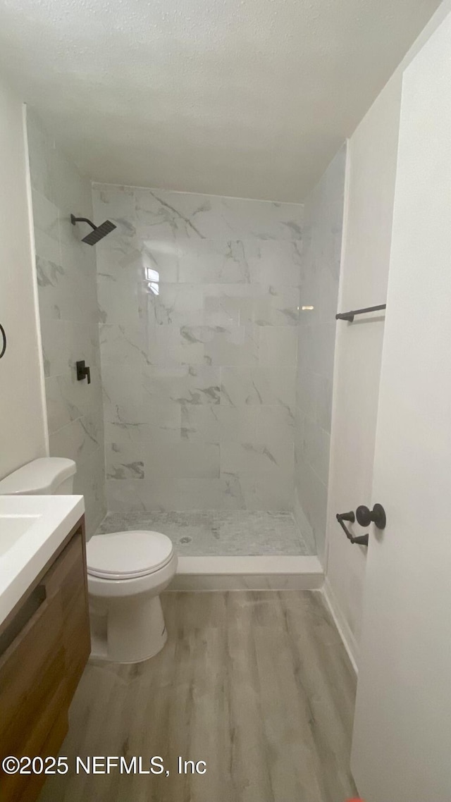 bathroom featuring wood-type flooring, vanity, tiled shower, toilet, and a textured ceiling