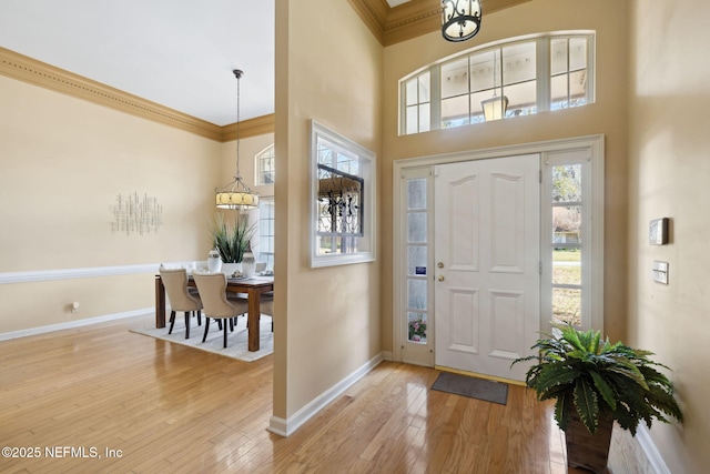 entrance foyer with crown molding, a towering ceiling, a chandelier, and hardwood / wood-style floors