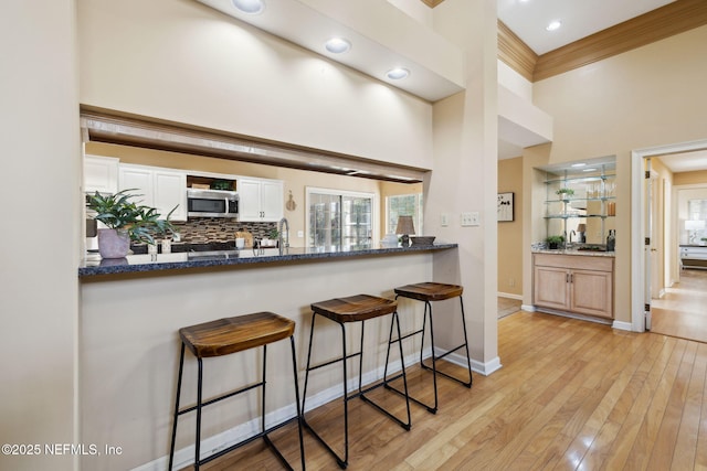 kitchen with white cabinetry, dark stone countertops, light hardwood / wood-style floors, decorative backsplash, and kitchen peninsula