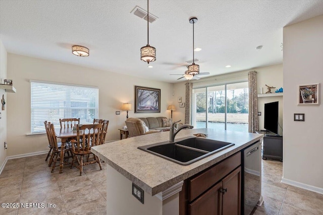 kitchen with a kitchen island with sink, sink, stainless steel dishwasher, and a textured ceiling