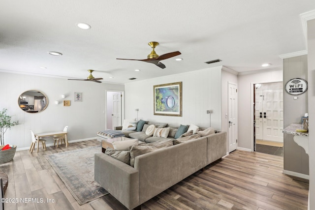 living area featuring a textured ceiling, wood finished floors, visible vents, baseboards, and ornamental molding