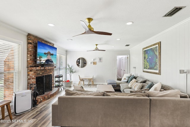 living room with ornamental molding, visible vents, a fireplace, and wood finished floors