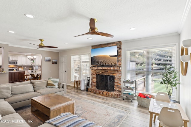 living room featuring ceiling fan, a textured ceiling, light wood-style flooring, a fireplace, and crown molding