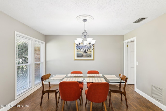 dining area featuring a textured ceiling, dark wood finished floors, visible vents, and a notable chandelier