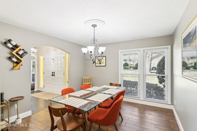 dining room with arched walkways, a notable chandelier, a textured ceiling, wood finished floors, and baseboards