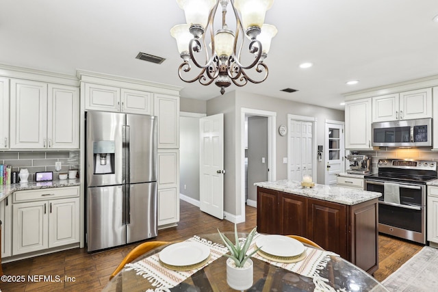 kitchen with tasteful backsplash, visible vents, appliances with stainless steel finishes, light stone counters, and dark wood-type flooring