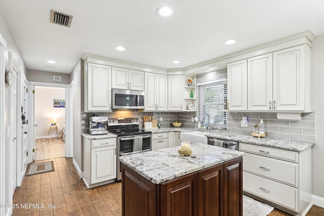 kitchen with visible vents, appliances with stainless steel finishes, wood finished floors, a sink, and backsplash