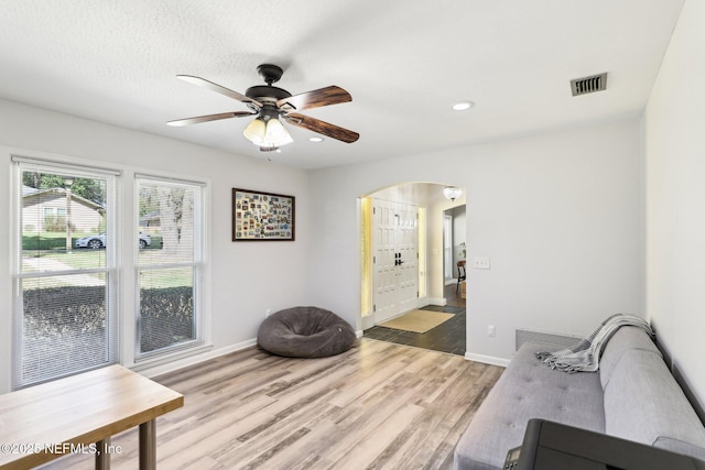 sitting room with arched walkways, light wood-type flooring, visible vents, and baseboards