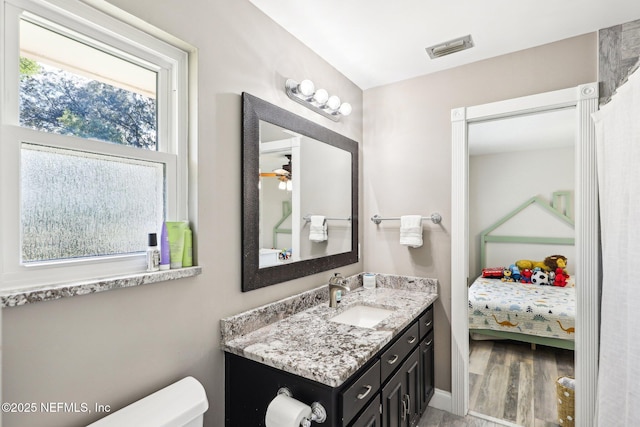 bathroom featuring toilet, wood finished floors, vanity, visible vents, and ensuite bath