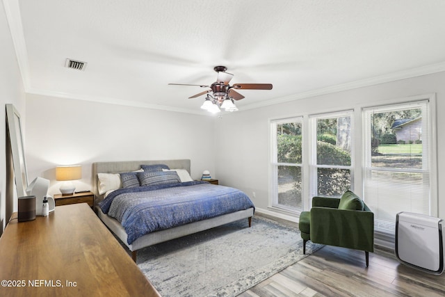 bedroom with ceiling fan, a textured ceiling, wood finished floors, visible vents, and crown molding