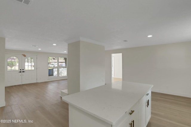 kitchen with a center island, light stone counters, white cabinets, and light wood-type flooring