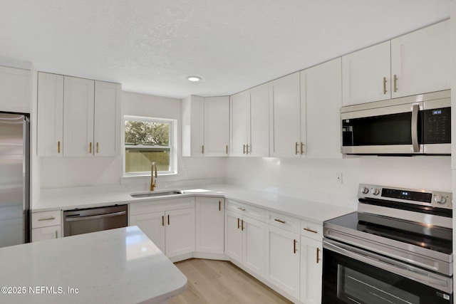 kitchen featuring sink, light hardwood / wood-style flooring, white cabinetry, stainless steel appliances, and a textured ceiling