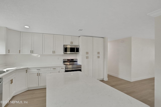 kitchen featuring light stone counters, stainless steel appliances, white cabinets, and light wood-type flooring