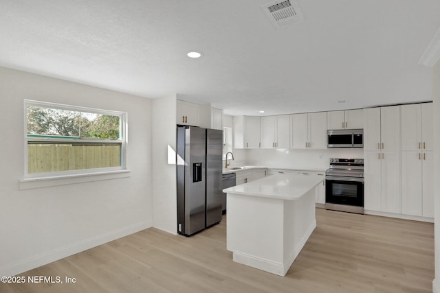 kitchen featuring sink, appliances with stainless steel finishes, a kitchen island, light hardwood / wood-style floors, and white cabinets