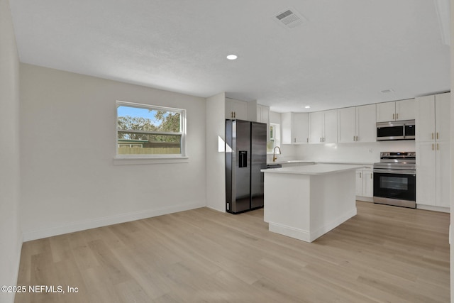 kitchen with white cabinetry, sink, a center island, stainless steel appliances, and light wood-type flooring