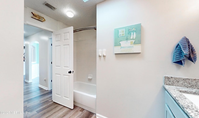 bathroom featuring wood-type flooring, bathtub / shower combination, a textured ceiling, and vanity