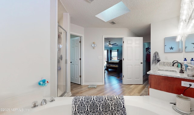 bathroom with a skylight, separate shower and tub, a textured ceiling, vanity, and hardwood / wood-style flooring