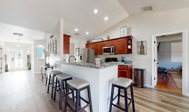 kitchen with light hardwood / wood-style floors, light stone countertops, kitchen peninsula, and appliances with stainless steel finishes