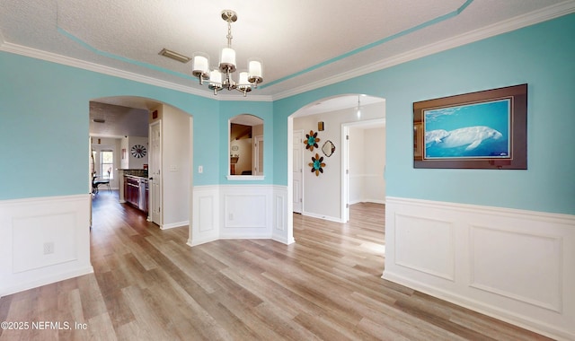 unfurnished dining area featuring ornamental molding, light hardwood / wood-style floors, a chandelier, and a textured ceiling