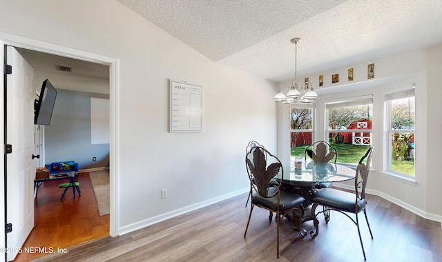 dining space with an inviting chandelier, wood-type flooring, and a textured ceiling