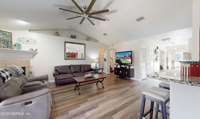 living room featuring a tile fireplace, lofted ceiling, light wood-type flooring, ceiling fan, and a textured ceiling