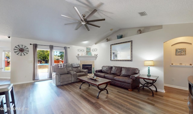 living room with lofted ceiling, hardwood / wood-style floors, a tile fireplace, and a textured ceiling