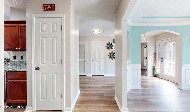 corridor with crown molding, a textured ceiling, and light hardwood / wood-style flooring