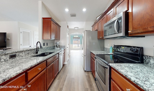 kitchen featuring appliances with stainless steel finishes, sink, light stone counters, a textured ceiling, and light hardwood / wood-style flooring