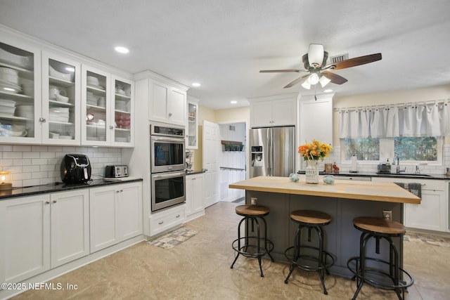 kitchen featuring appliances with stainless steel finishes, backsplash, white cabinets, and a kitchen breakfast bar